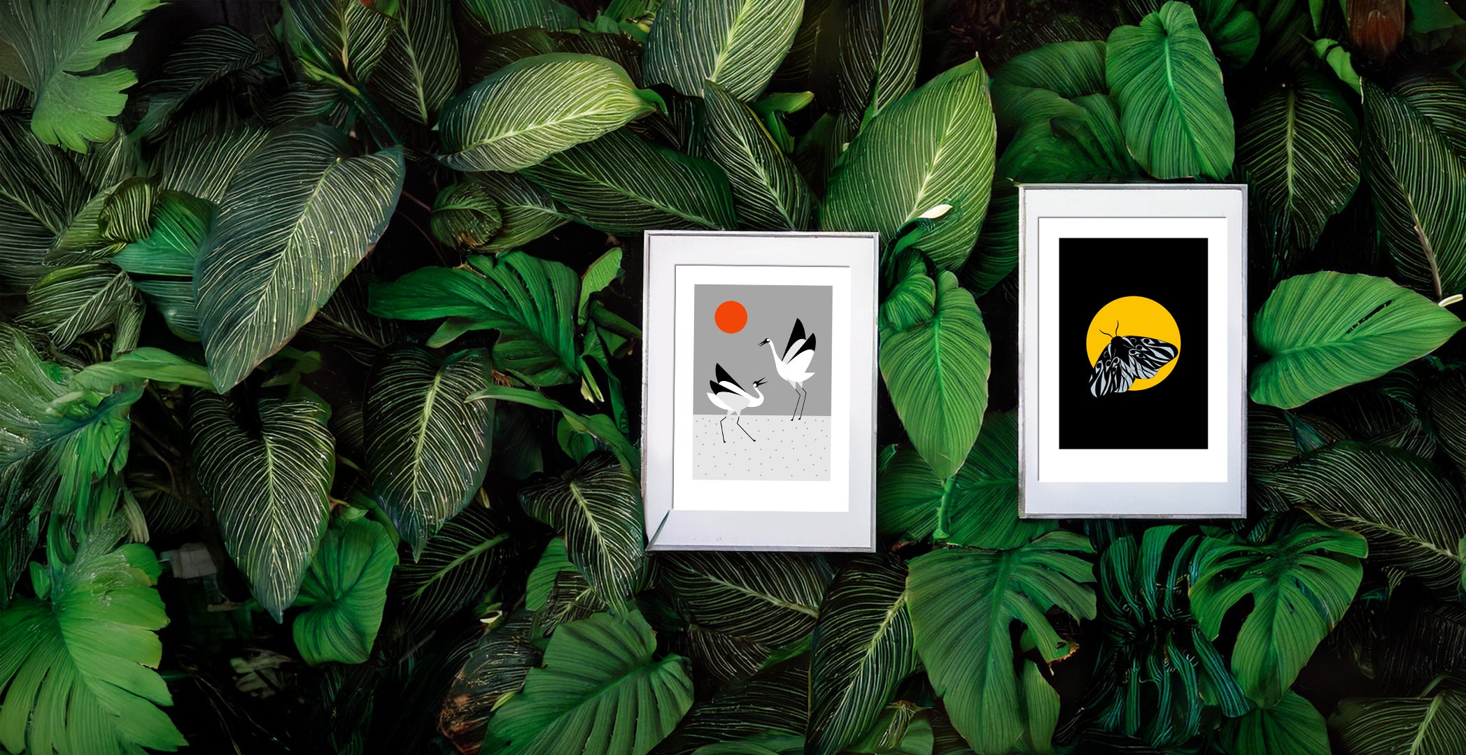 Two framed art prints nestled among lush green leaves